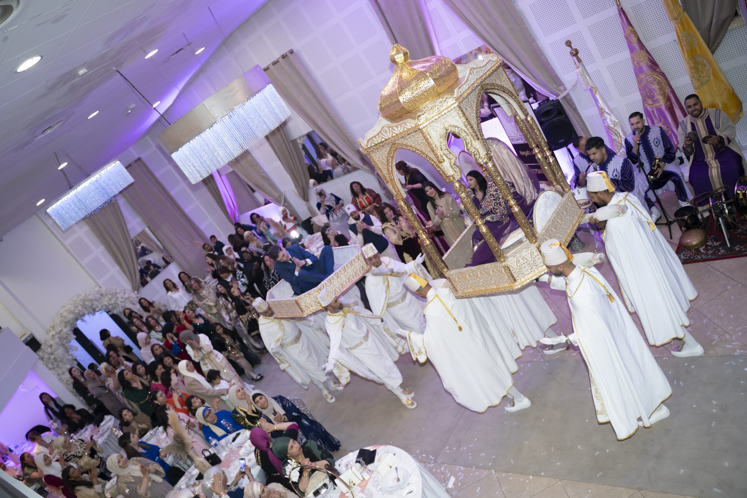 Salle de réception décorée avec canapé blanc, éclairage doré et compositions florales avant l'arrivée des invités