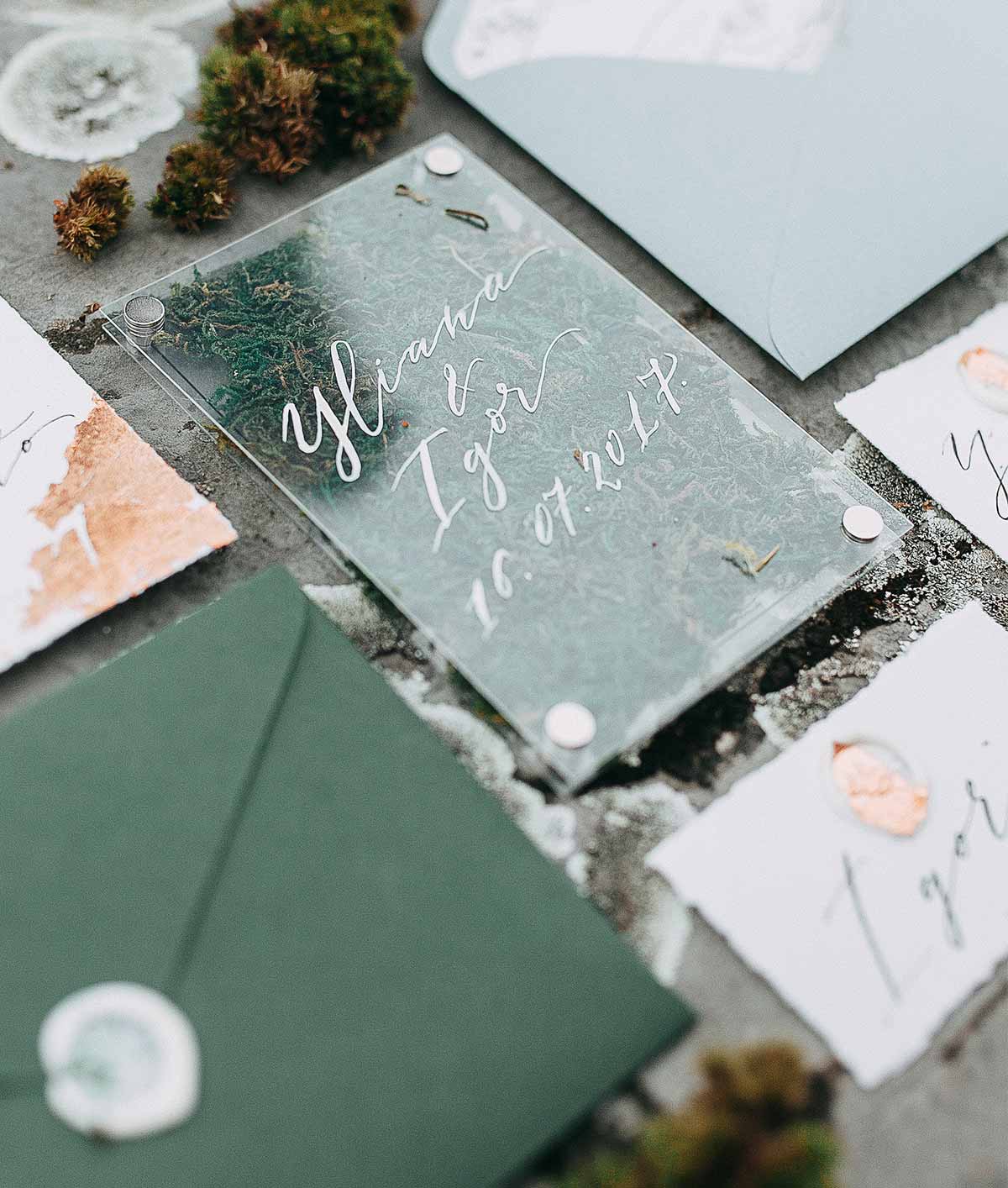 Carton d'invitation calligraphié posé sur une table avec enveloppes et éléments végétaux