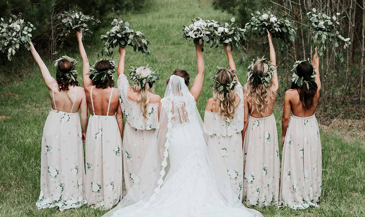 Mariée entourée de ses demoiselles d'honneur levant leurs bouquets de fleurs, vues de dos