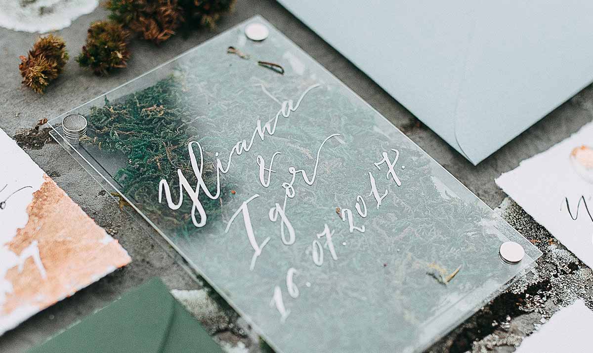 Carton d'invitation calligraphié posé sur une table avec enveloppes et éléments végétaux