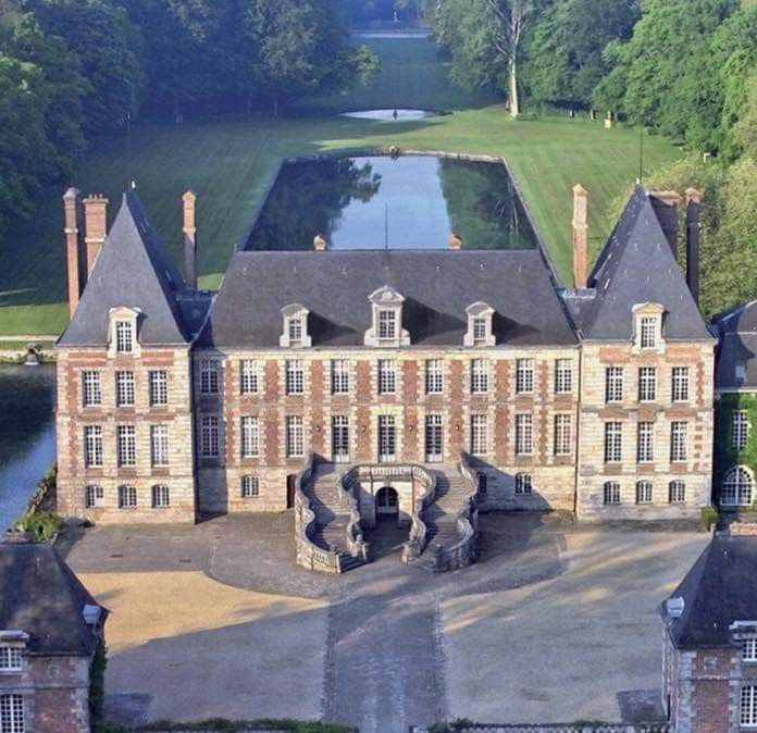 Vue aérienne d'un château en briques entouré d'un jardin à la française avec bassin
