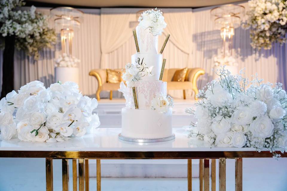 Pièce montée à quatre étages entourée de compositions florales blanches sur la table d'honneur