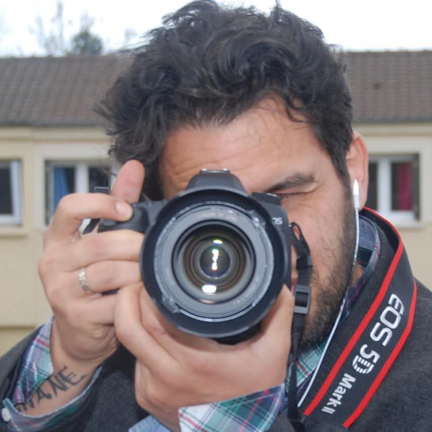 Man holding a DSLR camera up to his eye, taking a photo, with a red and black EOS 50D strap visible.